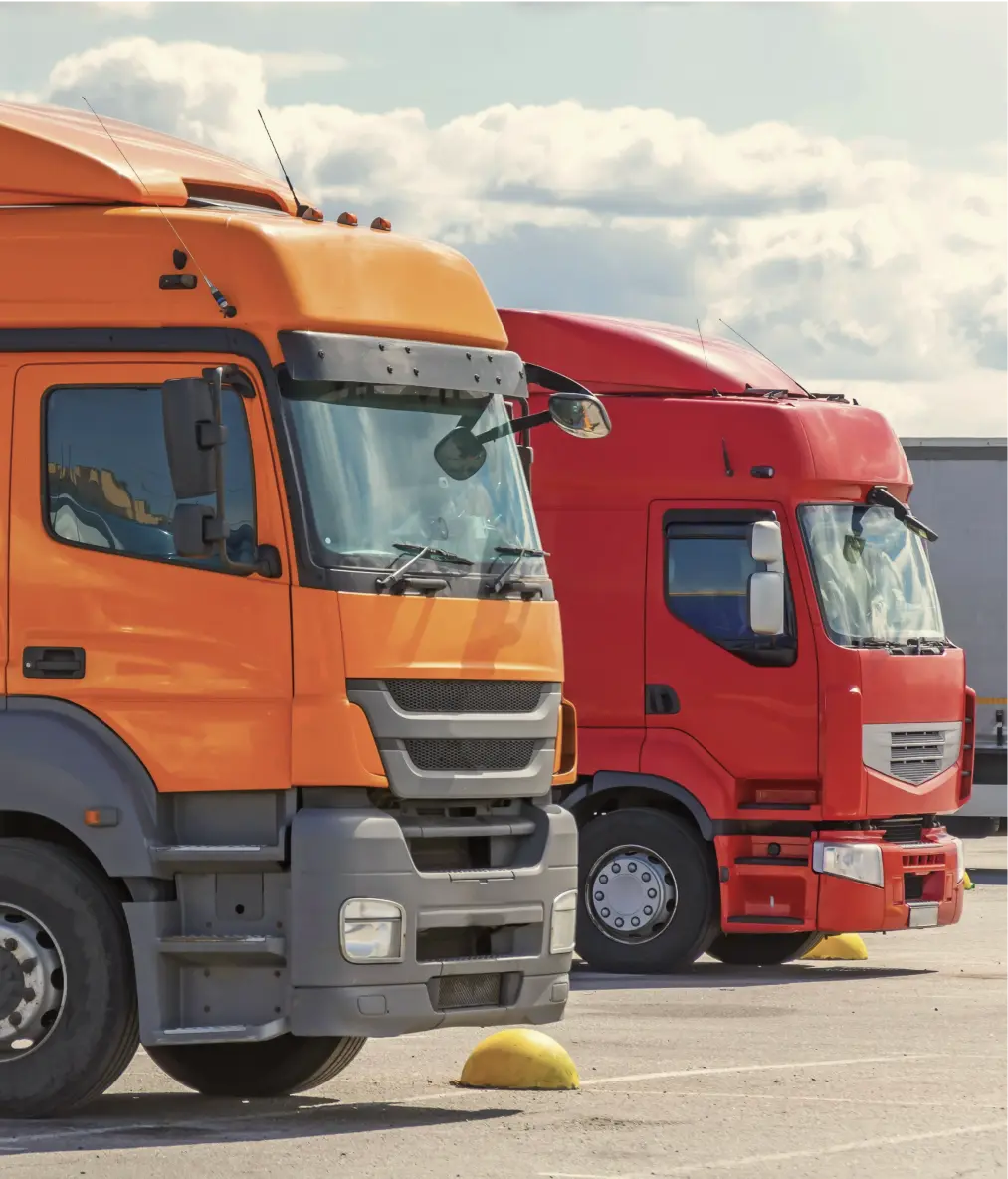 Orange and red semi-trucks parked side by side in a lot under a cloudy sky.